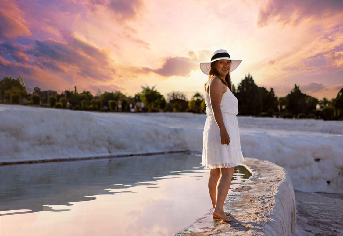 A woman turns to smile at the camera under a brilliant rose sunrise in Pamukkale