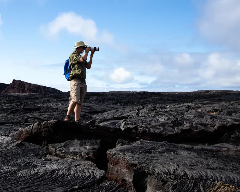 A photographer stands on black lava rock under blue skies while taking a photo in the Galapagos Islands