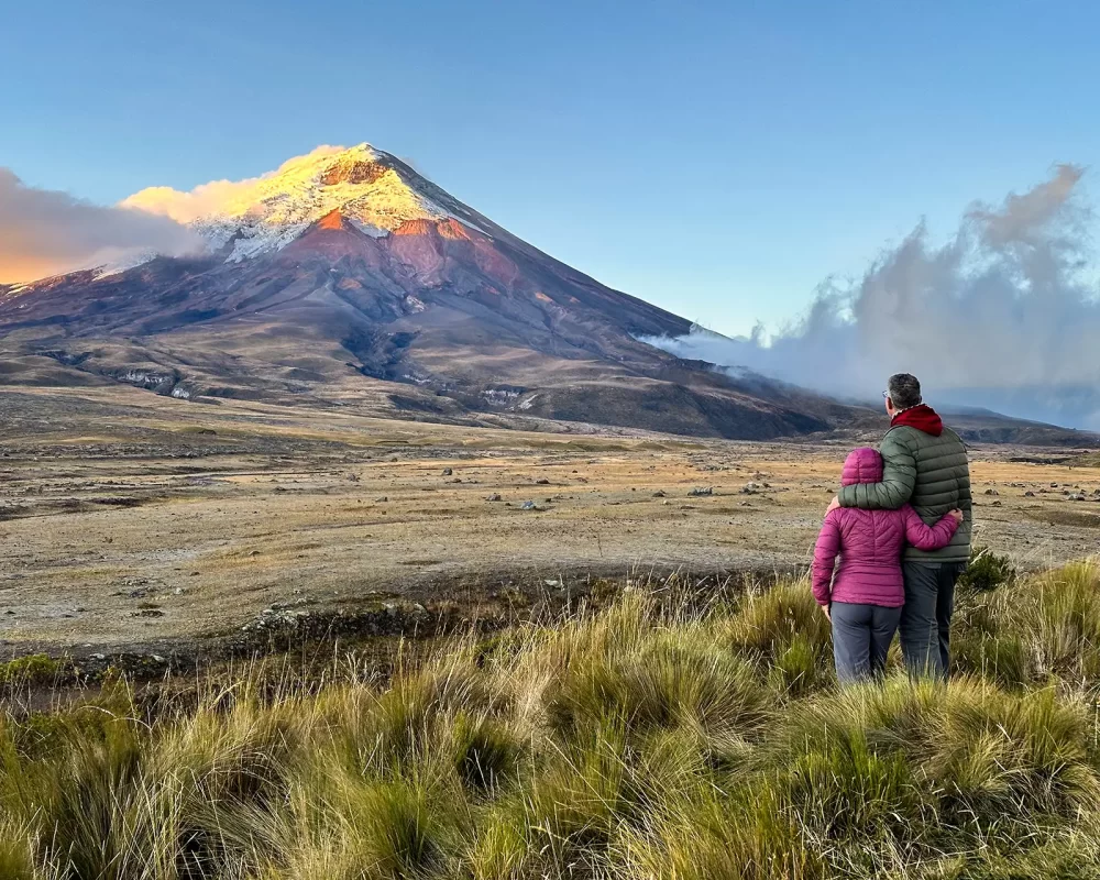 A man and woman embrace at dawn while looking out over Cotopaxi Volcano
