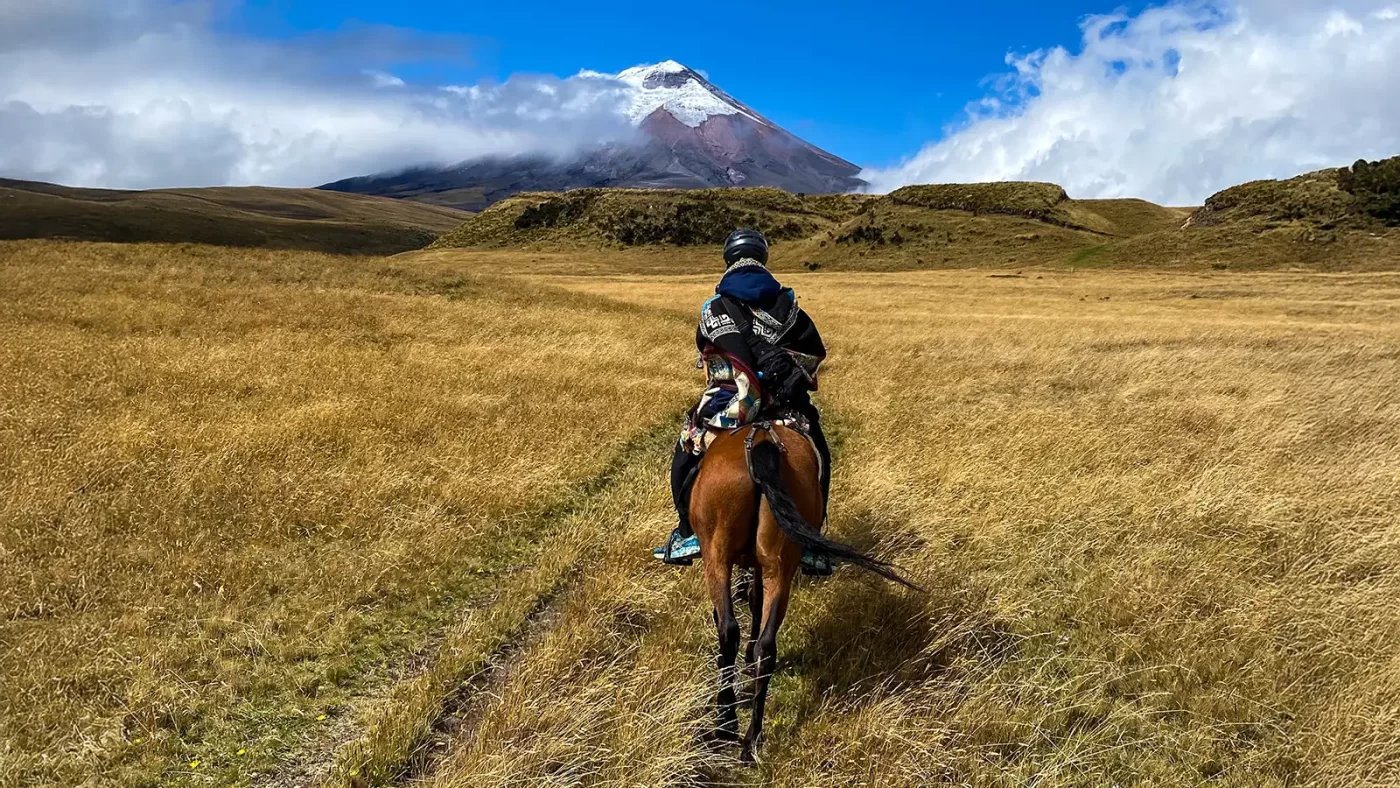 A boy rides a horse across a field of grass in Cotopaxi National Park