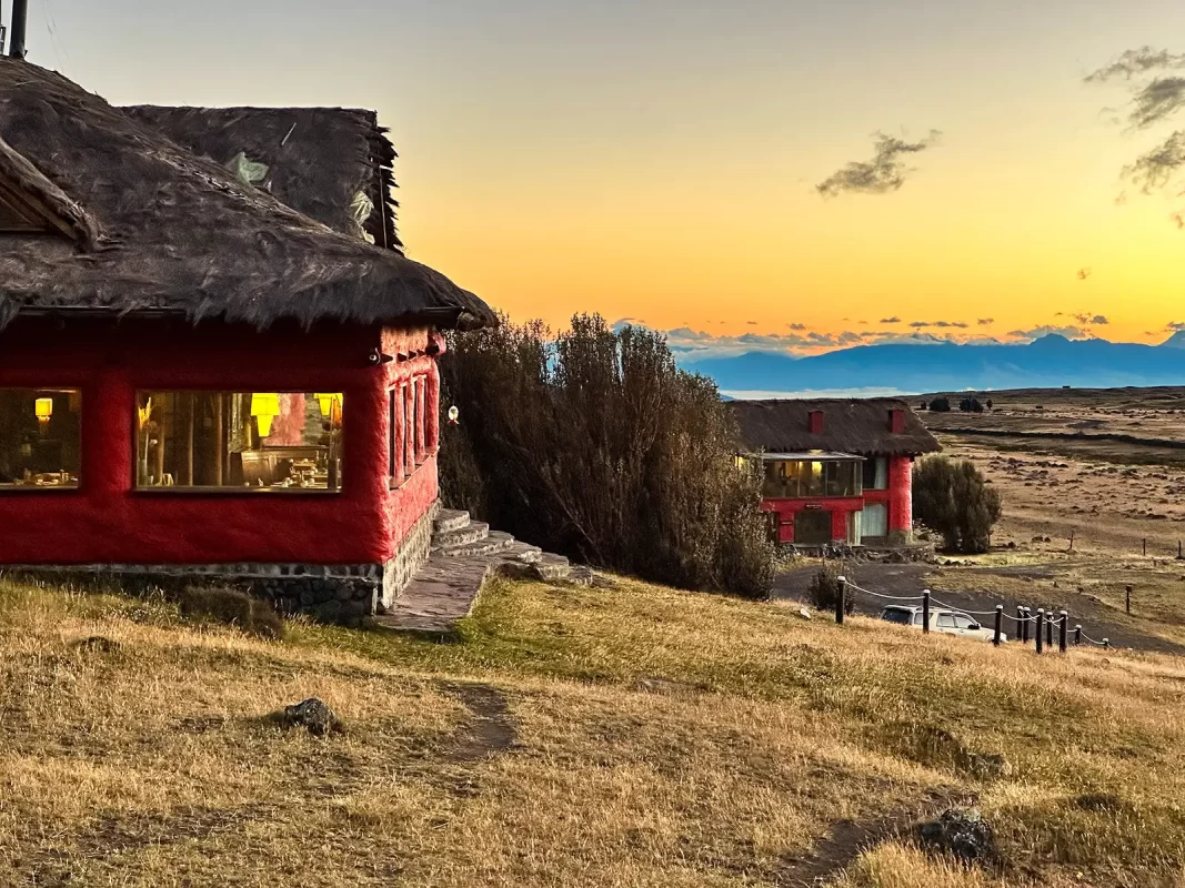 A red lodge with a thatch roof on a hill of grass at sunset - Tambopaxi Lodge at sunset