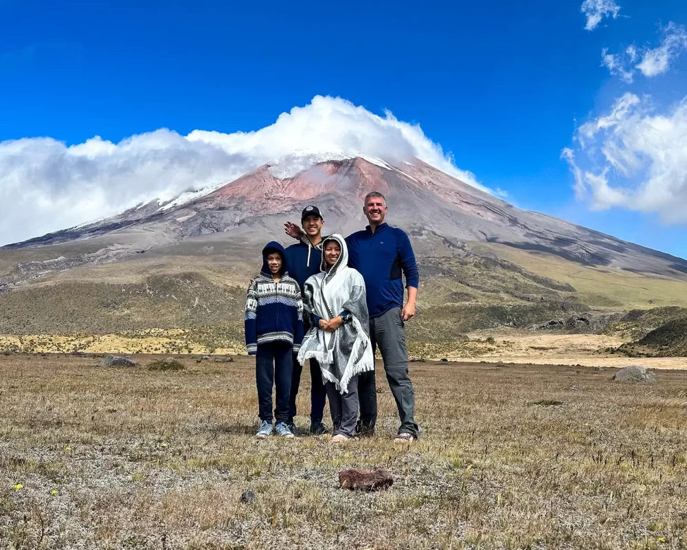 A family stands proudly in a grassy field in front of Cotopaxi Volcano