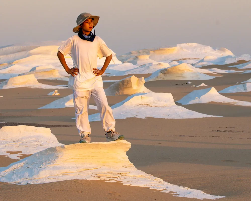 A boy wearing white clothes stands on a white rock in the white desert in Egypt